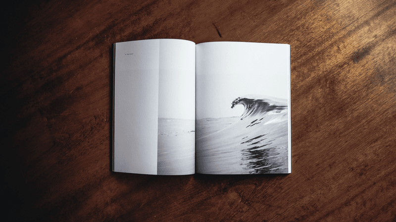 Book on a wood table opened to a page with an ocean wave. 